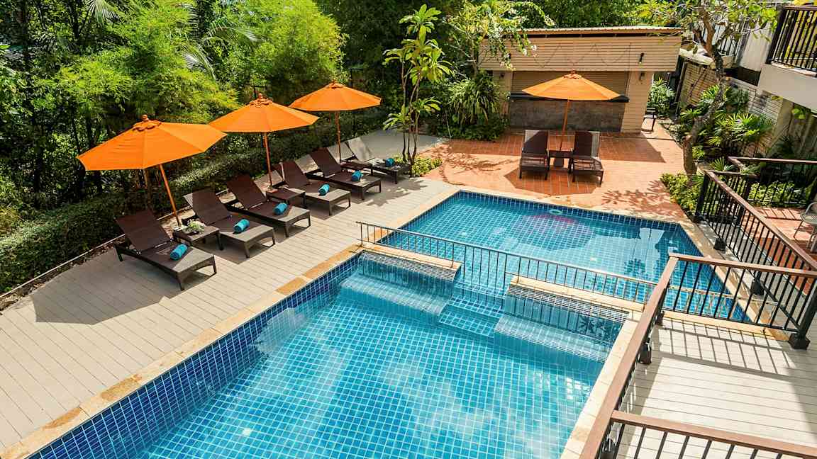 En pool med blått kakel omgiven av solstolar och orangea parasoller. (AI-genererad text)