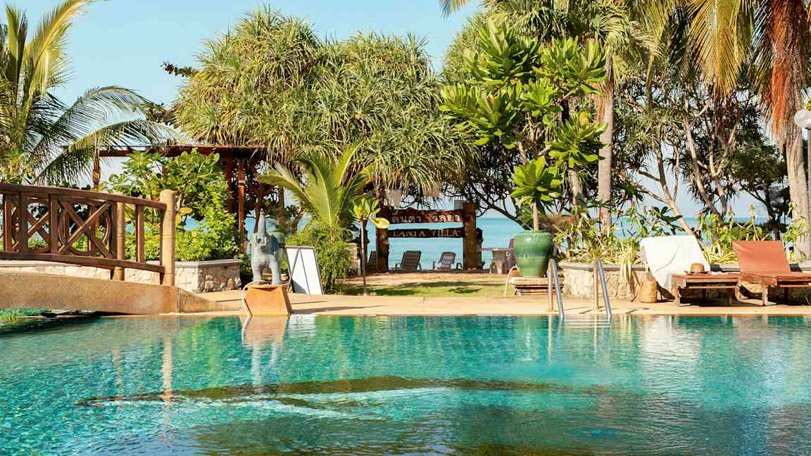 En pool med solstolar intill, och bakom finns träd och en skylt med texten 'Lanta Villa'. (AI-genererad text)