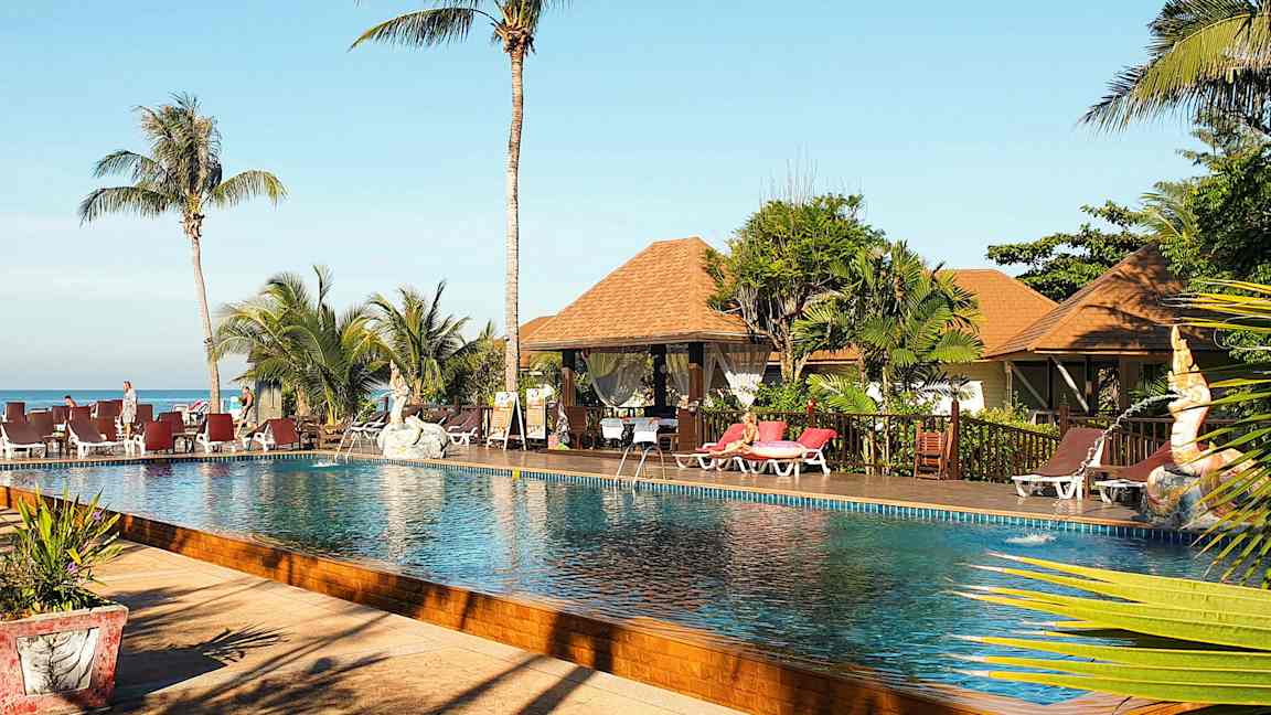 Bild av en poolområde med palmer, solstolar och bungalow-liknande byggnader i bakgrunden. (AI-genererad text)