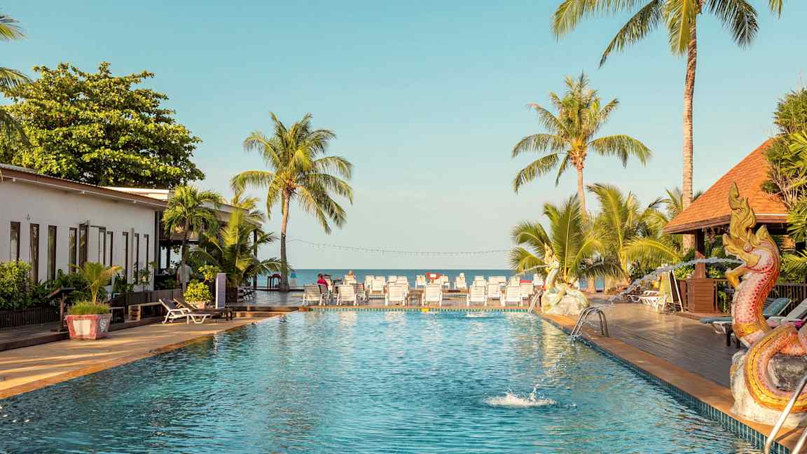 Utomhuspool med palmer och solsängar i bakgrunden, samt en dekoration föreställande en drake bredvid poolen. (AI-genererad text)