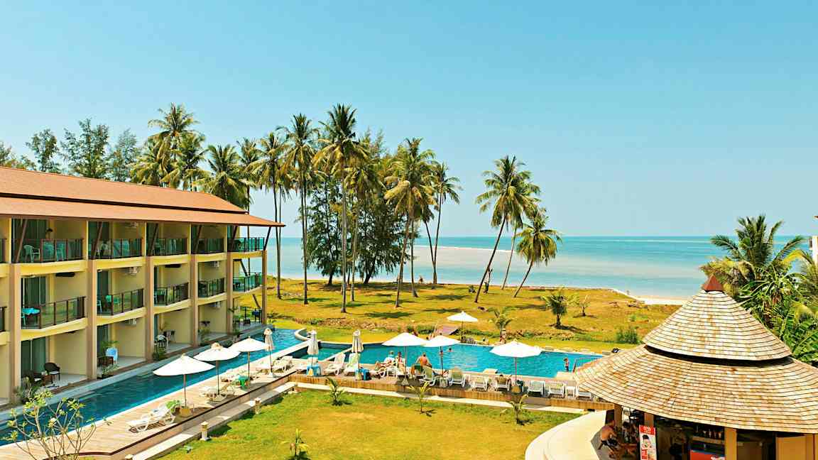 En resort med en pool, solstolar och parasoller, nära stranden med palmer. (AI-genererad text)