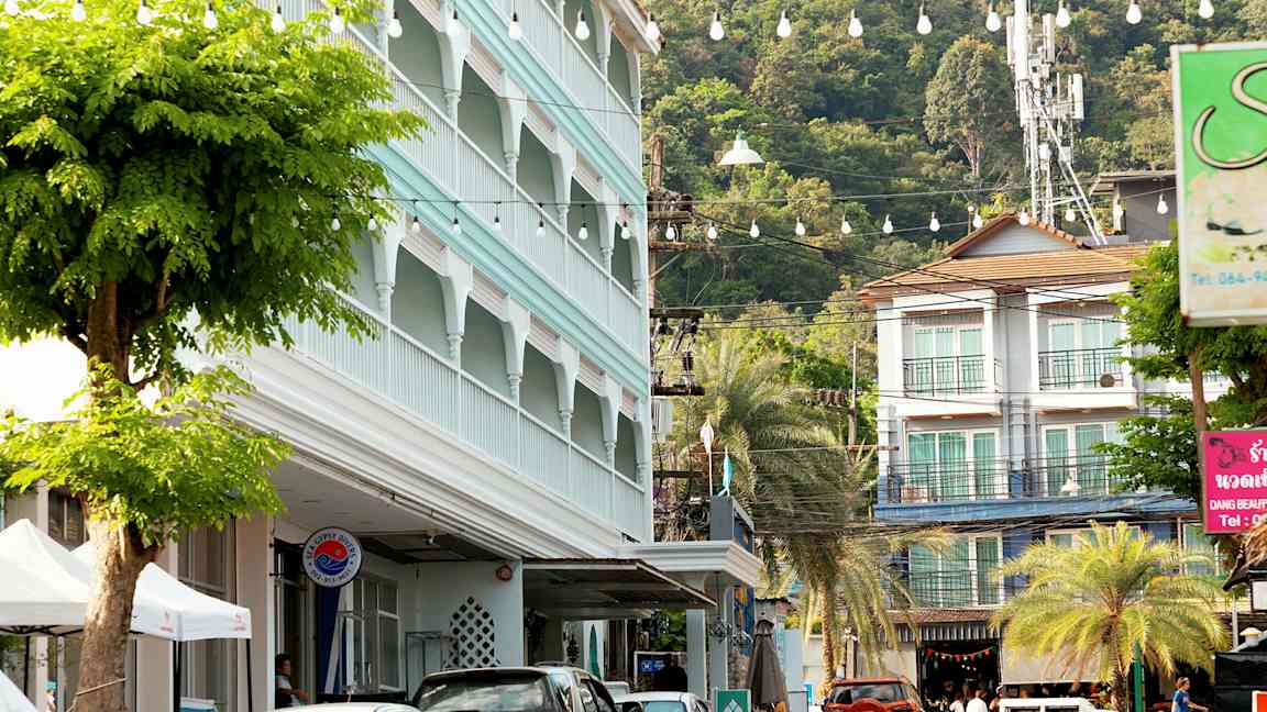 Gatuvy med parkerade bilar, en byggnad med blå fasad och grönskande träd. (AI-genererad text)