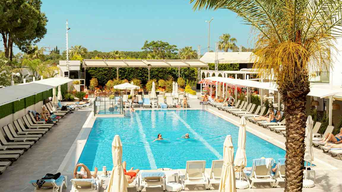 Bild av en pool omgiven av solstolar och parasoller, med personer som badar och solar. (AI-genererad text)