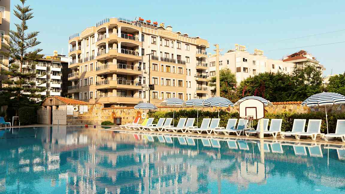 Bild av en pool med solstolar och parasoller vid sidan, samt en byggnad i bakgrunden. (AI-genererad text)