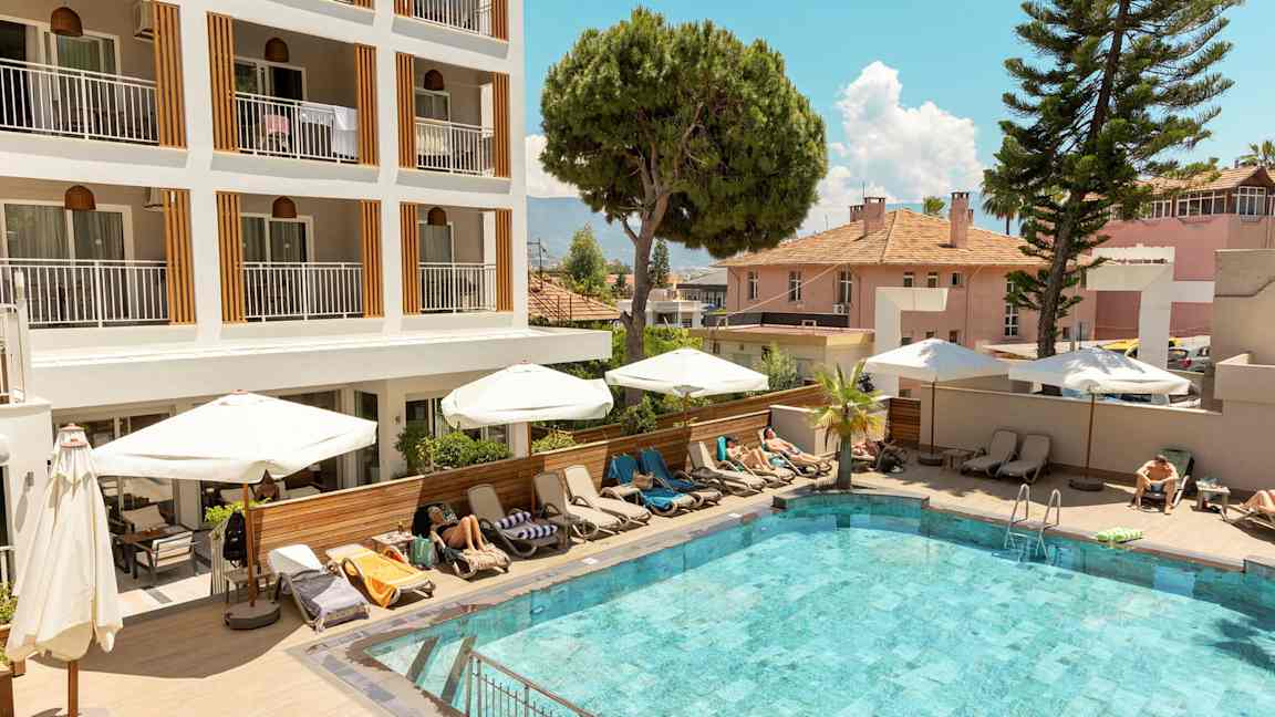 Utomhuspool framför ett hotell med solstolar och parasoller. (AI-genererad text)