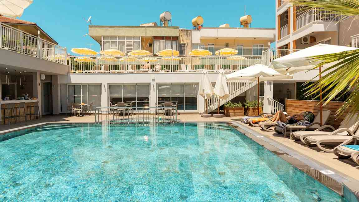 En utomhuspool omgiven av solstolar och parasoller på ett hotell. (AI-genererad text)
