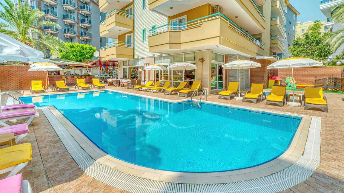 En utomhuspool omgiven av solstolar och parasoller framför en hotellbyggnad. (AI-genererad text)