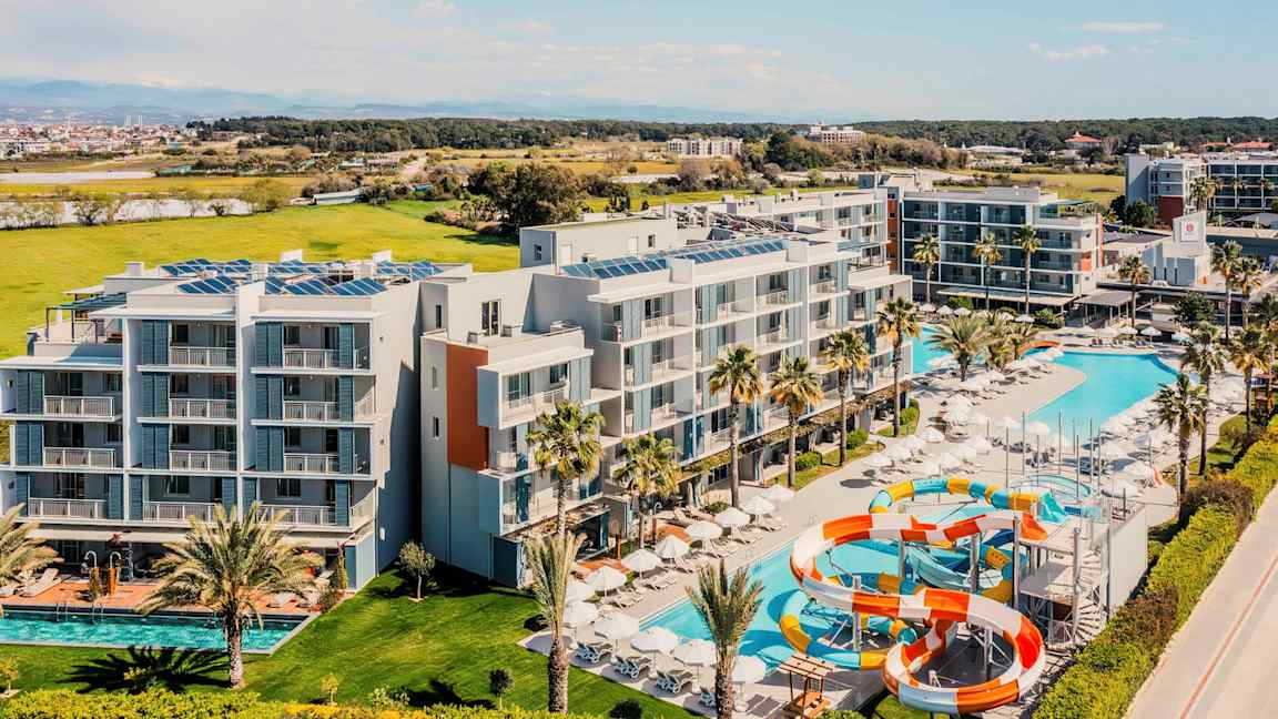 Flygfoto av ett hotell med pooler och vattenrutschbanor, omgiven av grönområden. (AI-genererad text)