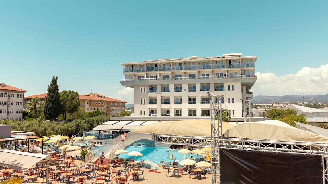 En bild av ett hotell med flera våningar, en poolområdet med solstolar, parasoller och ett rekreationsområde. (AI-genererad text)
