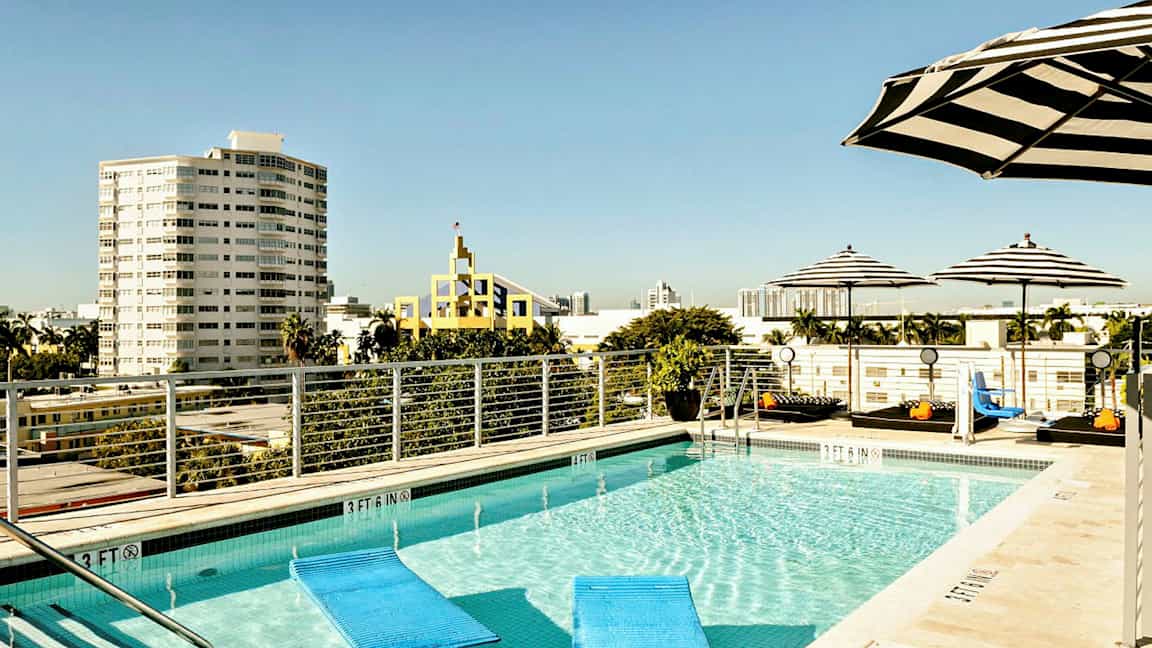 En takpool omgiven av randiga parasoller, med en stadsutsikt och flera byggnader i bakgrunden. (AI-genererad text)