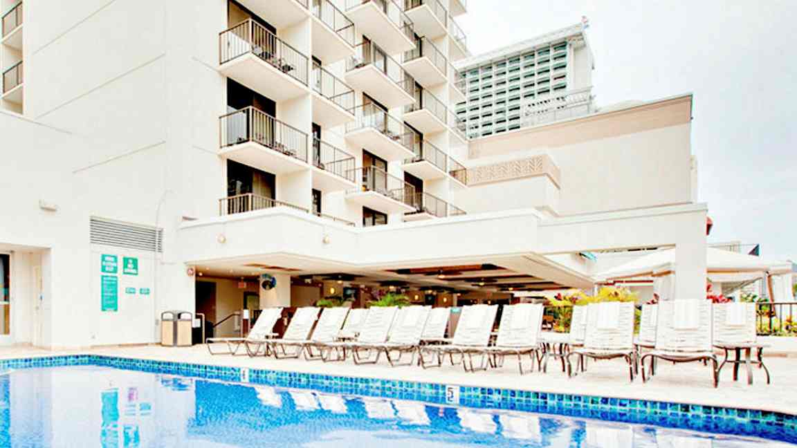 Bild av en byggnad med balkonger, en pool och solstolar. (AI-genererad text)
