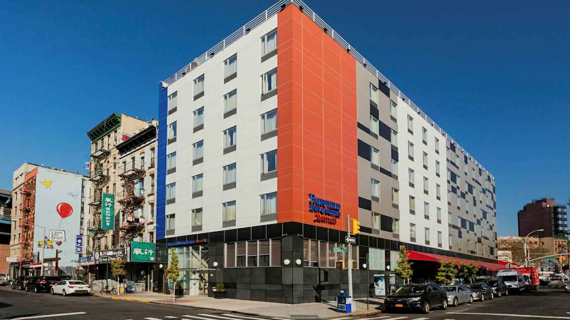 En modern byggnad i ett hörn av ett stadsområde, med en livlig gata och trafik samt omgivande äldre byggnader. (AI-genererad text)