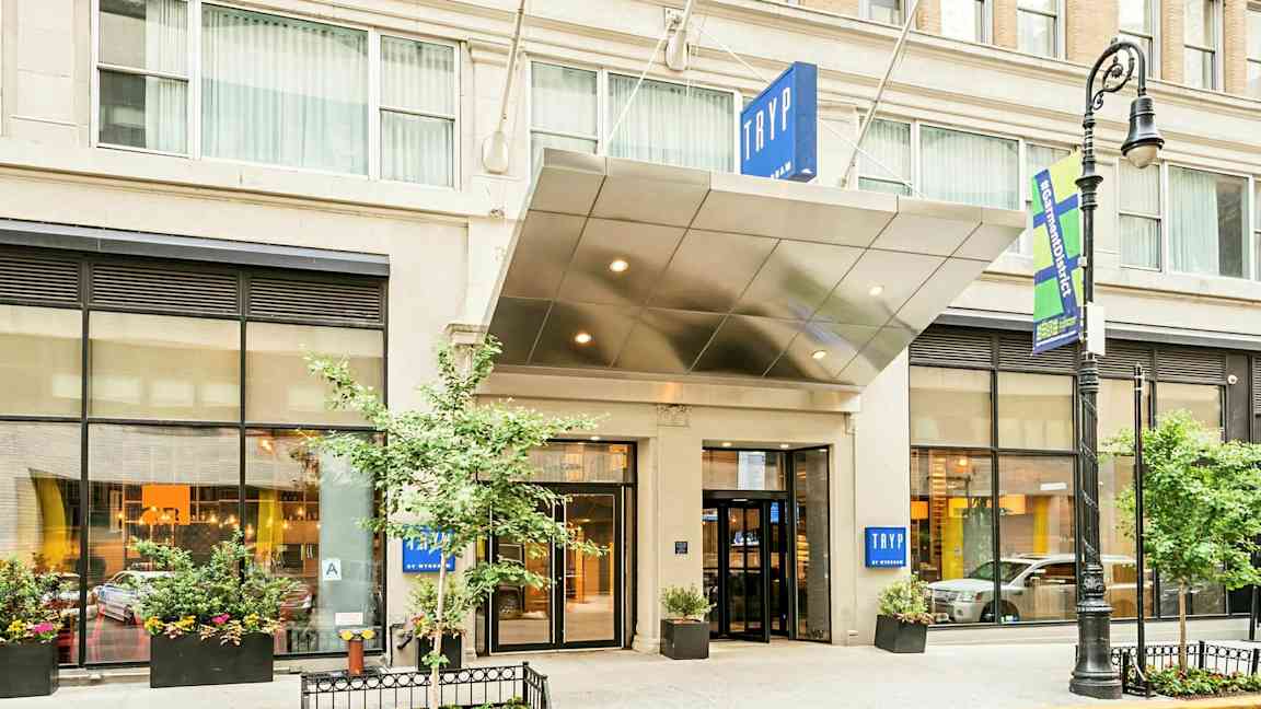 Entré till ett hotell med skylt texten "TRYP". Byggnaden har stora fönster och planteringar. (AI-genererad text)