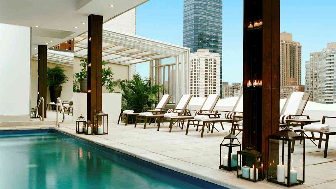 En modern utomhuspool med solsängar och tända lyktor i en stadsmiljö. (AI-genererad text)