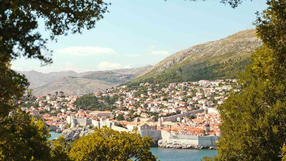 En vy över Dubrovnik med sin historiska stadsmur, omgiven av grönska. (AI-genererad text)