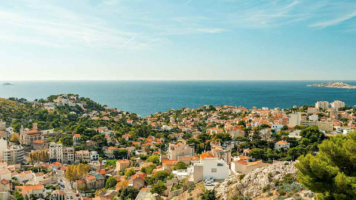 Utsikt över en kuststad med röda tak och grönska, samt havet i bakgrunden. (AI-genererad text)