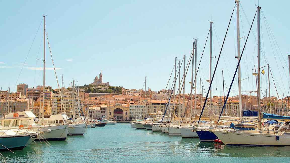 En marina med segelbåtar och en stad i bakgrunden. (AI-genererad text)