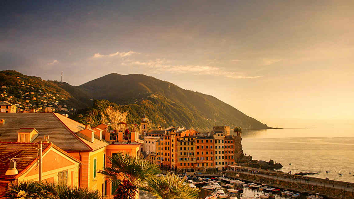 Bild av en kuststad vid havet med små båtar i hamnen och berg i bakgrunden. (AI-genererad text)