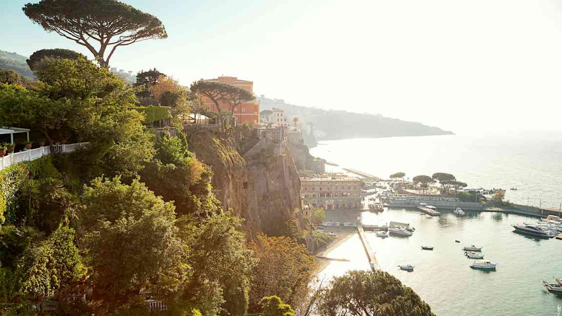 Utsikt från klippa över hamn med båtar och byggnader. (AI-genererad text)