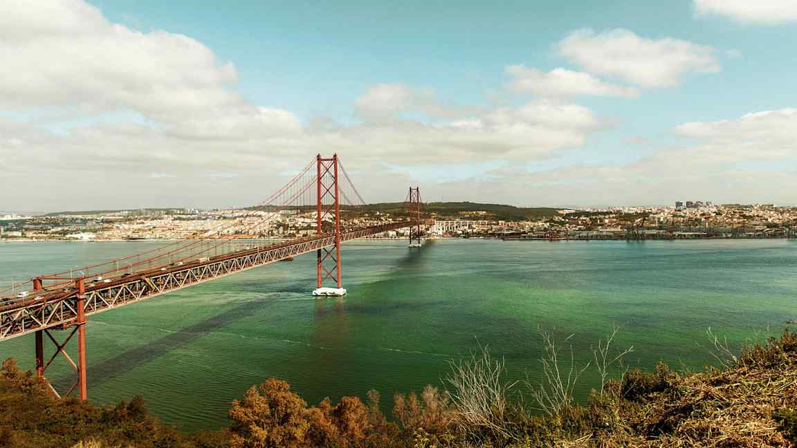 På bilden syns en röd bro över vatten med en stad i bakgrunden. (AI-genererad text)