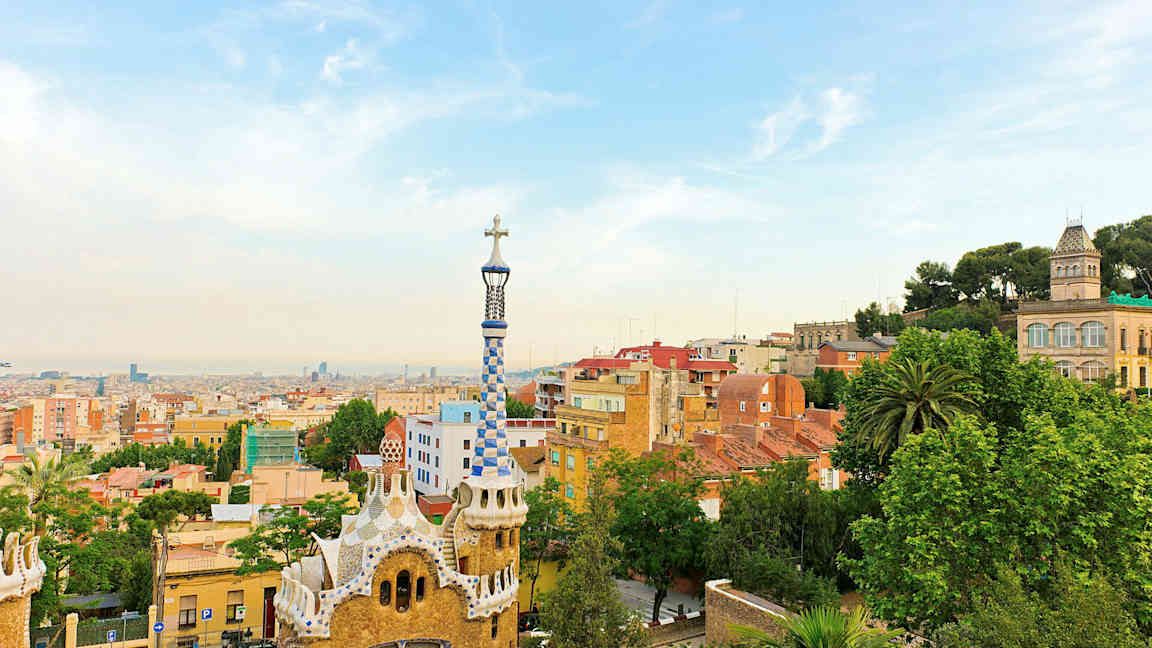 Vy över Park Güell i Barcelona med färgglada byggnader och stadens skyline i bakgrunden. (AI-genererad text)