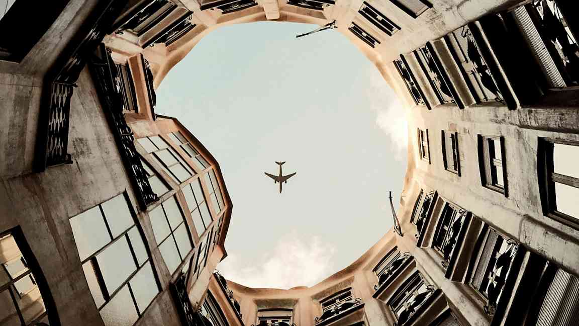 En bild av en flygplanssiluett mot himlen sedd från innergården av en byggnad. (AI-genererad text)