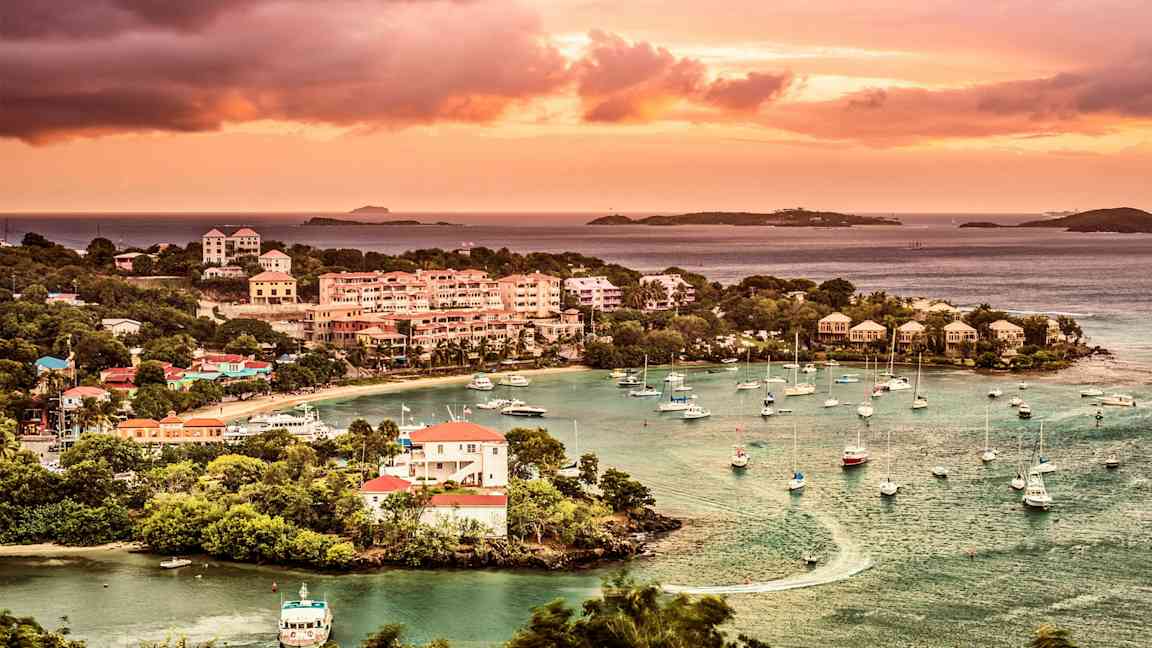 Bild av en kuststad med båtar vid en marina, omgivna av gröna träd och solnedgång i bakgrunden. (AI-genererad text)