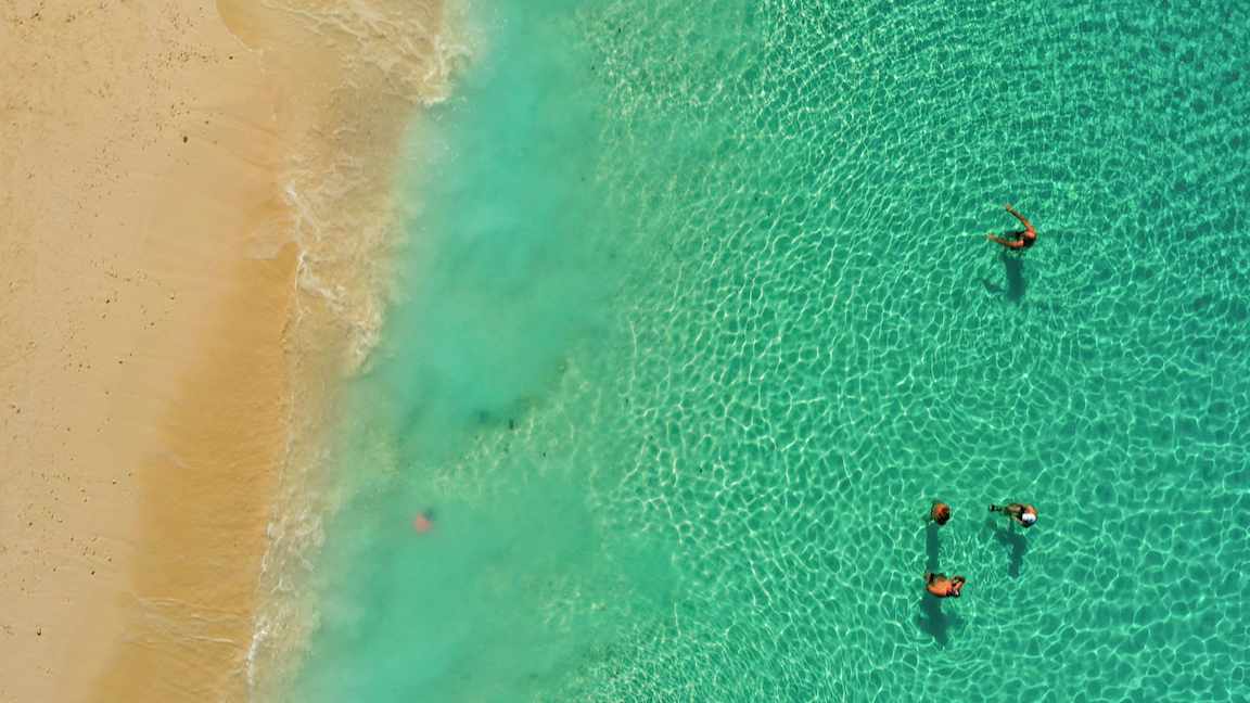 Flygfoto av personer som simmar i havet nära en sandstrand. (AI-genererad text)