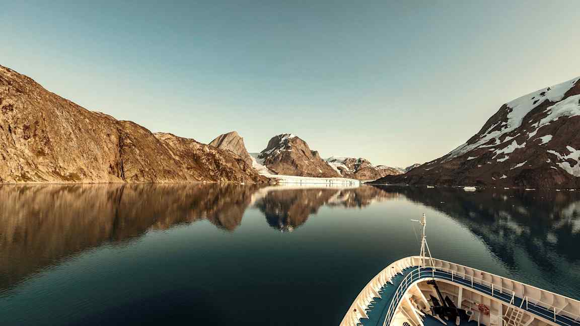 Ett fartyg i en lugn fjord omgiven av berg med snö. (AI-genererad text)