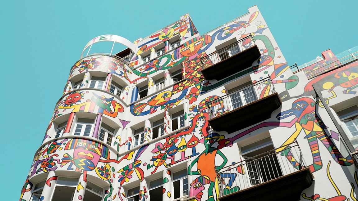 Byggnad med färgglada abstrakta målningar på fasaden mot en klarblå himmel. (AI-genererad text)