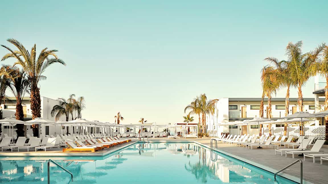 En swimmingpool omgiven av solstolar och palmer vid ett hotell. (AI-genererad text)