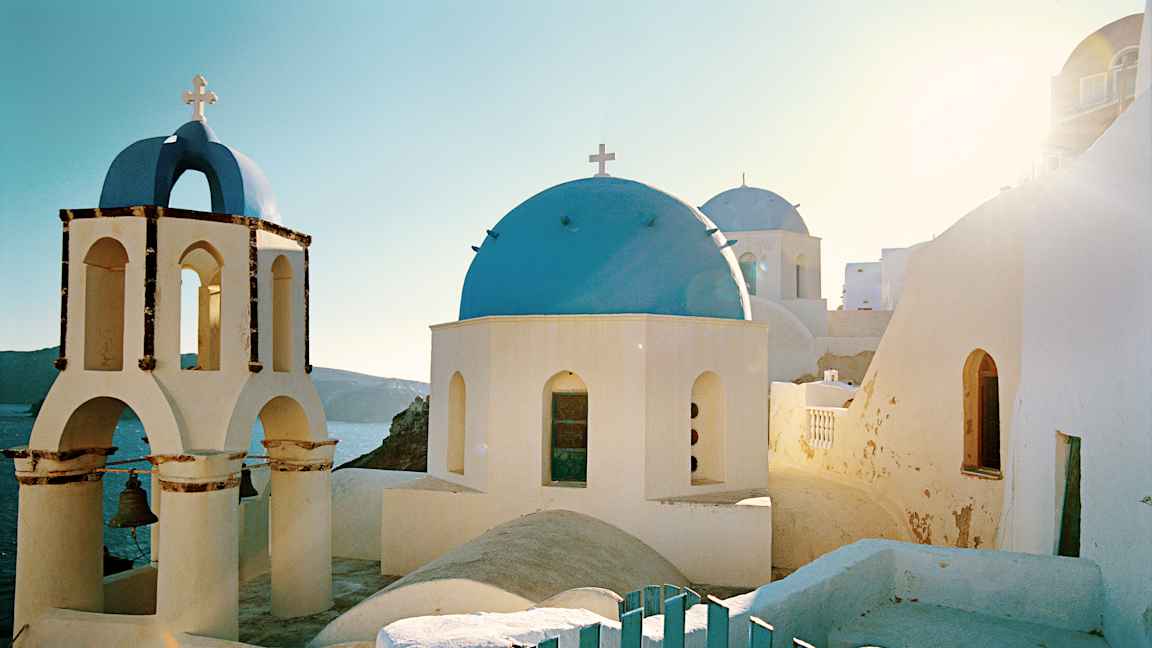 En vit byggnad med blå kupol och klocktorn i soligt landskap. (AI-genererad text)