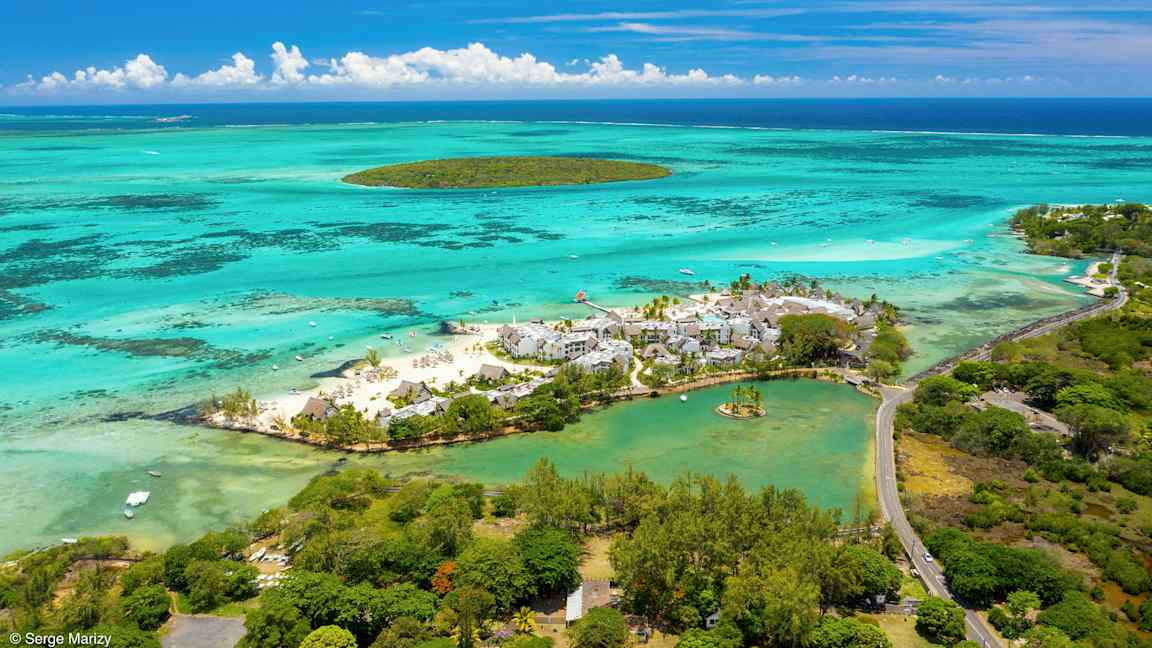 Flygbild över en strandresort omgiven av turkost vatten och grönska. (AI-genererad text)