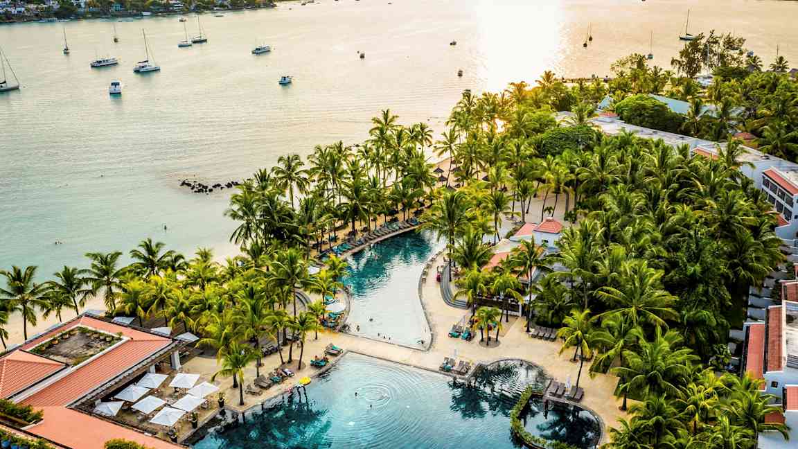 En strandresort med en pool omgiven av palmer och solstolar nära havet. (AI-genererad text)