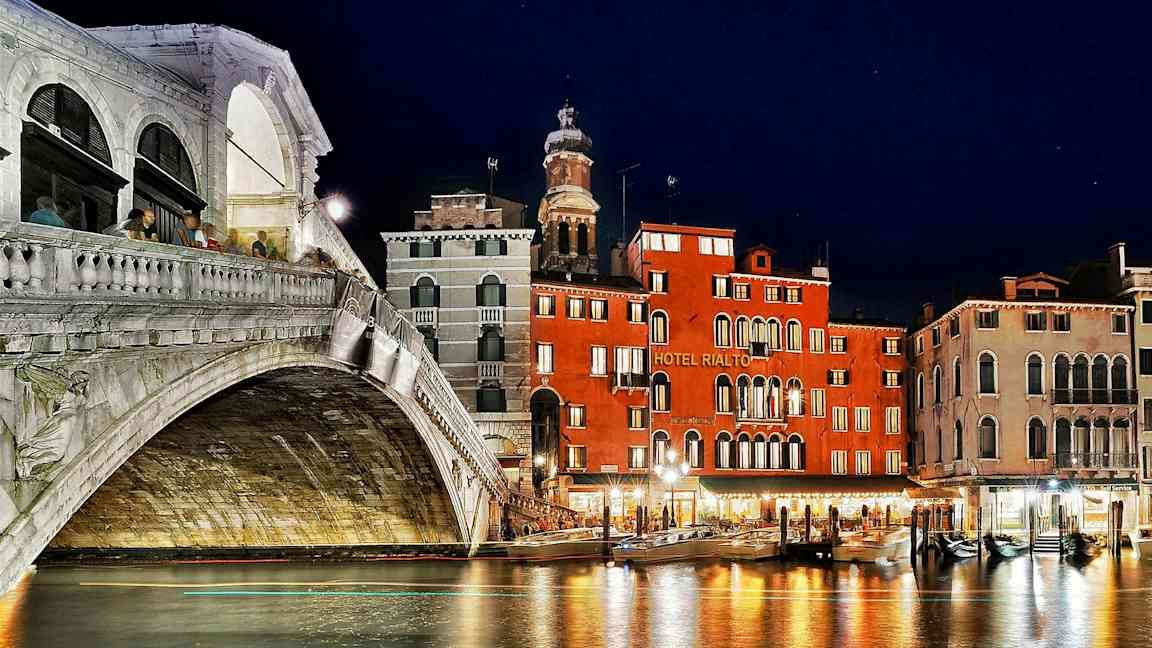 En nattvy av Rialtobron och intilliggande byggnader vid Grand Canal i Venedig. (AI-genererad text)