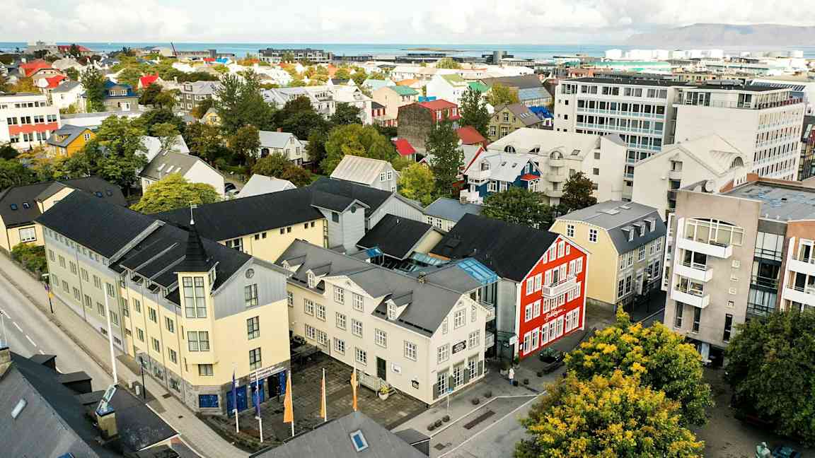 En stadsbild med färgglada byggnader, träd och en väg, samt bakgrund med hav och berg. (AI-genererad text)