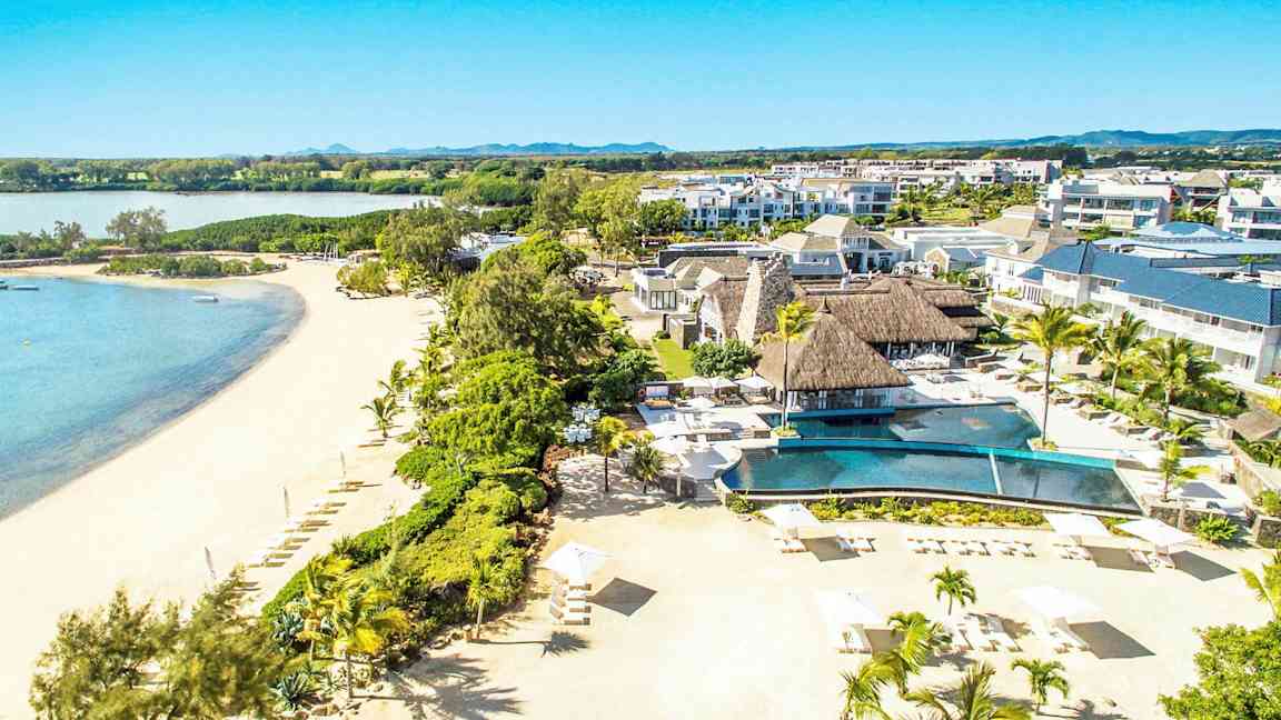 Flygfoto av en resort vid en sandstrand med palmer och en pool. (AI-genererad text)