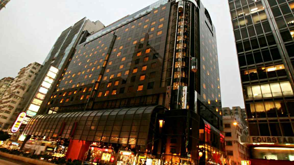 Ett upplyst flervåningshus i en stadsmiljö med glasfasad och gatuliv i förgrunden. (AI-genererad text)