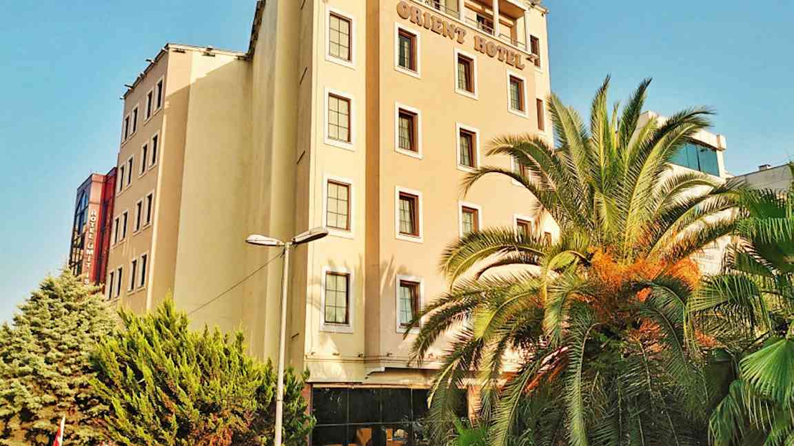 En hotellbyggnad med flera våningar. Det finns palmer och gröna träd framför byggnaden. (AI-genererad text)