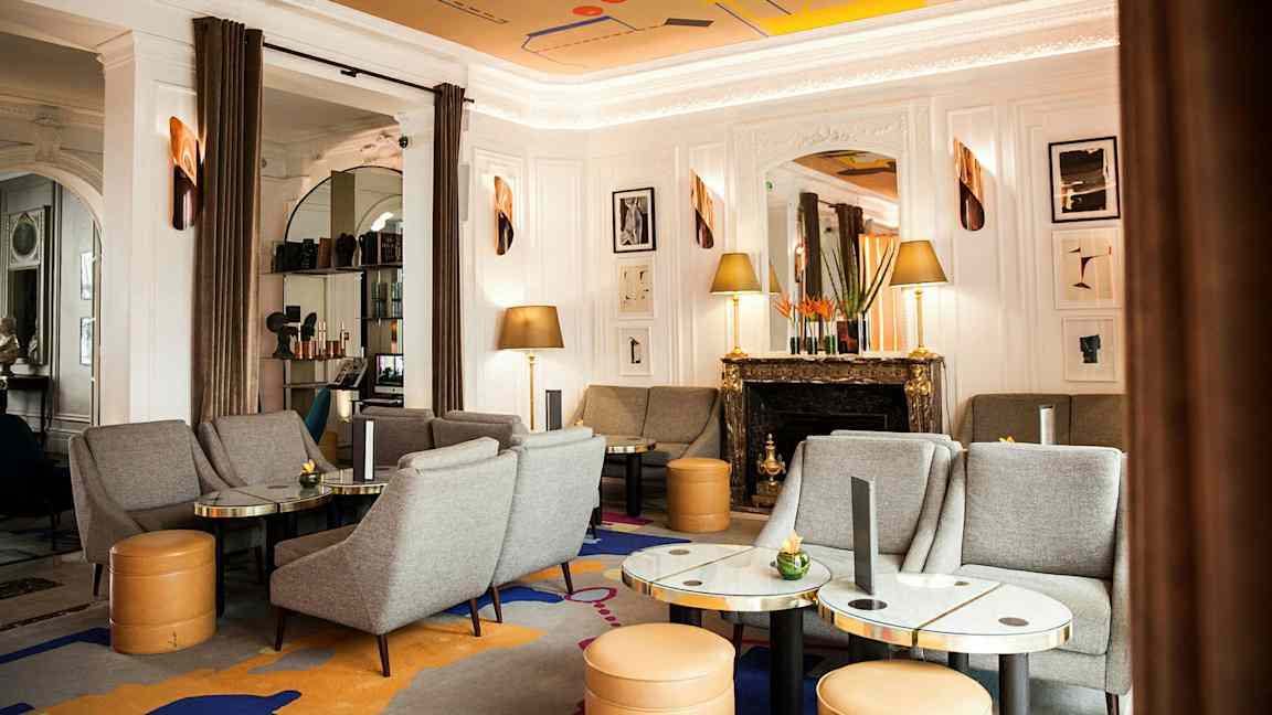 Ett elegant vardagsrum med grå soffor och fåtöljer, marmorbord, en dekorativ eldstad och konstverk på väggen. (AI-genererad text)