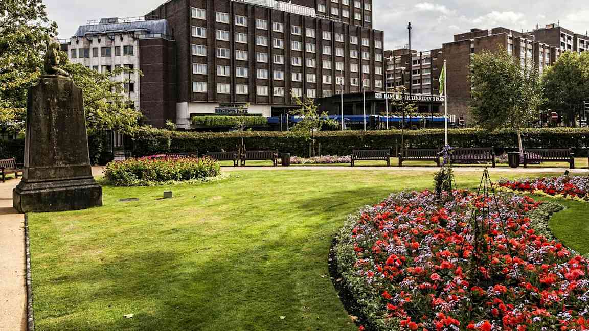En park med blommor och gräsmatta framför en byggnad. (AI-genererad text)
