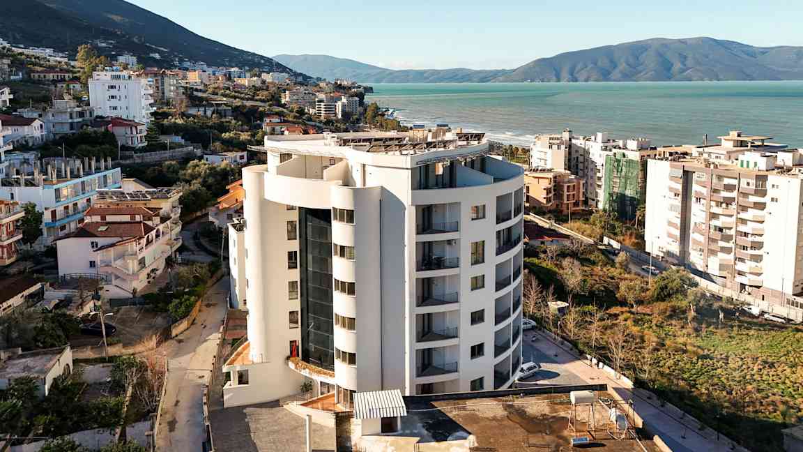 Ett höghus nära havet med omgivande byggnader och grönska. (AI-genererad text)