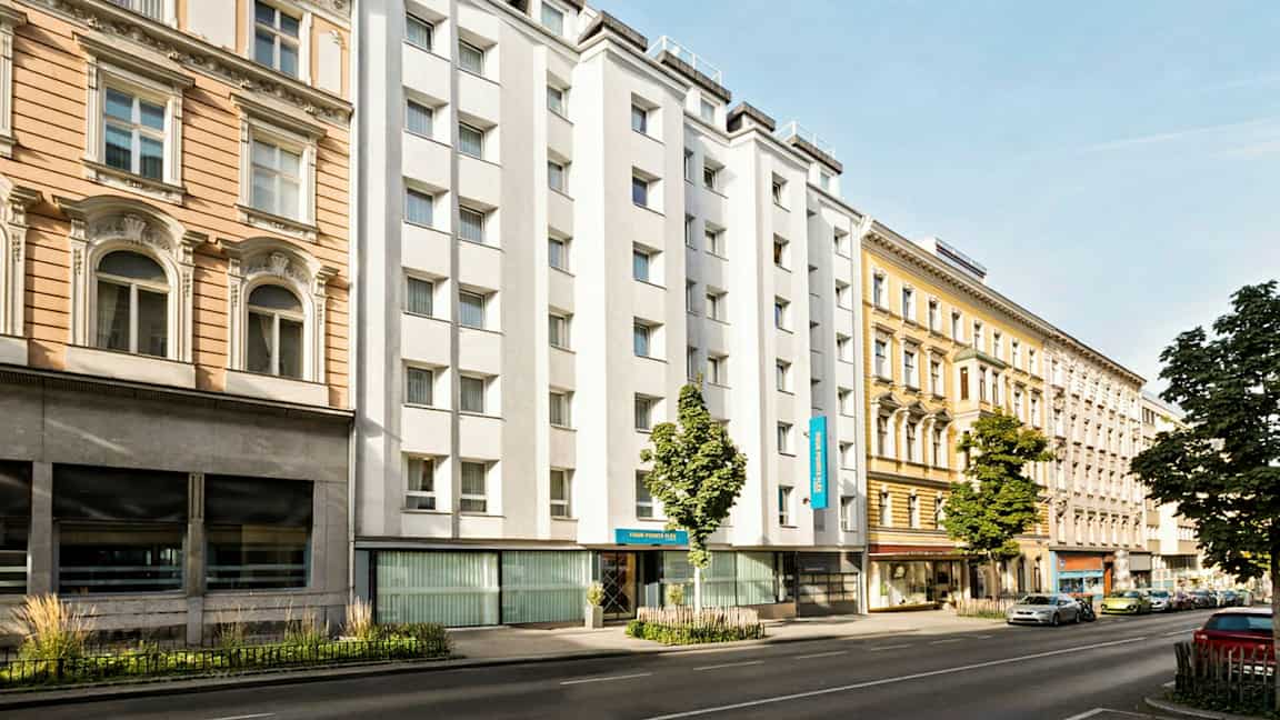 En stadsgata med byggnader från olika årtionden, inklusive ett hotell med vit fasad. (AI-genererad text)