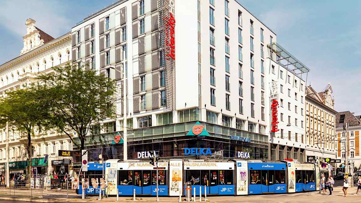 En flerfärgad spårvagn framför ett modernt hotell i stadslandskap. (AI-genererad text)