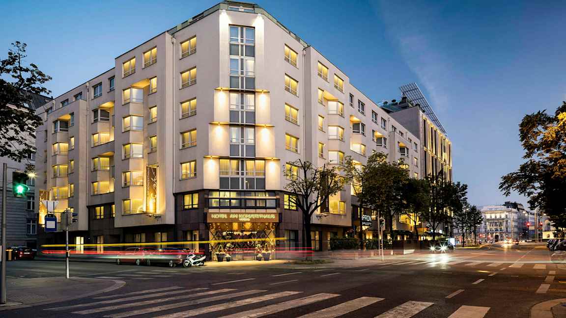 En byggnad som är upplyst på kvällen, med flera våningar och fönster, belägen vid en korsning. (AI-genererad text)