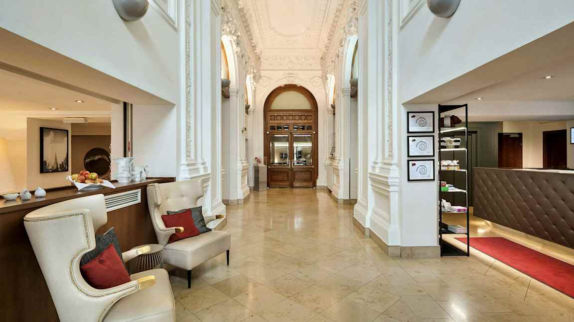 Ett elegant entrérum med marmorgolv, dekorativa takdetaljer och träportar. (AI-genererad text)