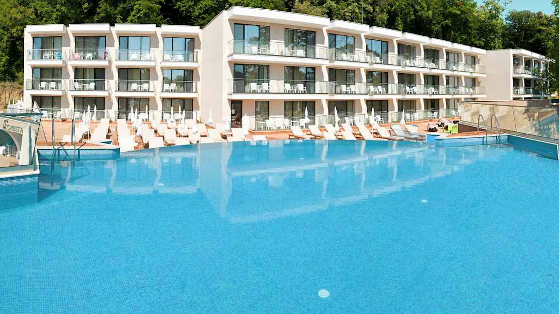 Hotellkomplex med en stor pool framför och solstolar runt omkring. (AI-genererad text)