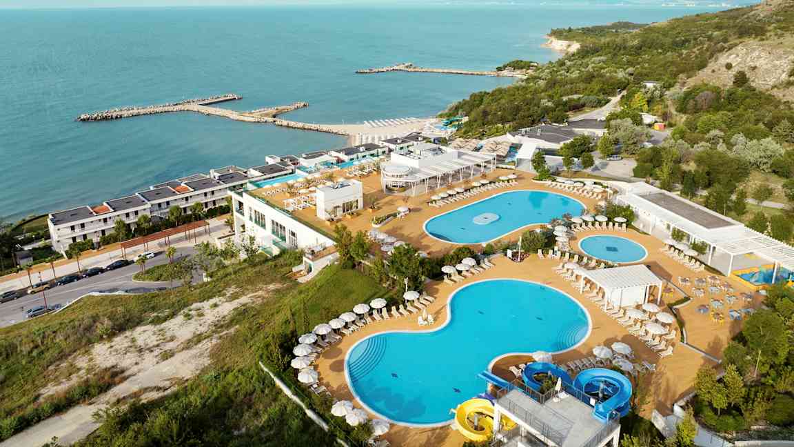 Bild av en resort vid havet med pooler, solstolar och en grönskande omgivning. (AI-genererad text)