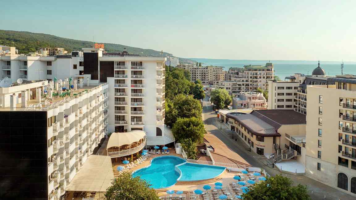 Hotellbyggnader med en utomhuspool och solstolar, omgivna av andra byggnader nära havet. (AI-genererad text)