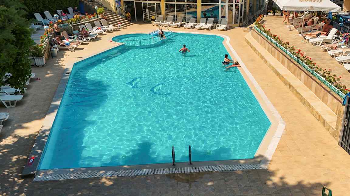 Ett sommarhotellpoolområde med solsängar och människor som badar i poolen. (AI-genererad text)
